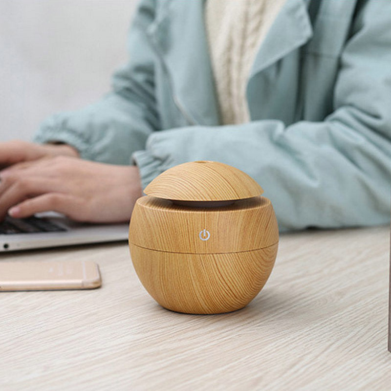 Wooden diffuser on a desk with a person using a laptop in the background