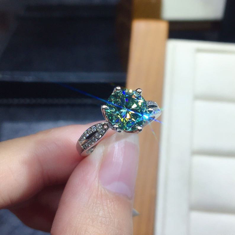 Ring with a large green gemstone held by a hand against a blurred background