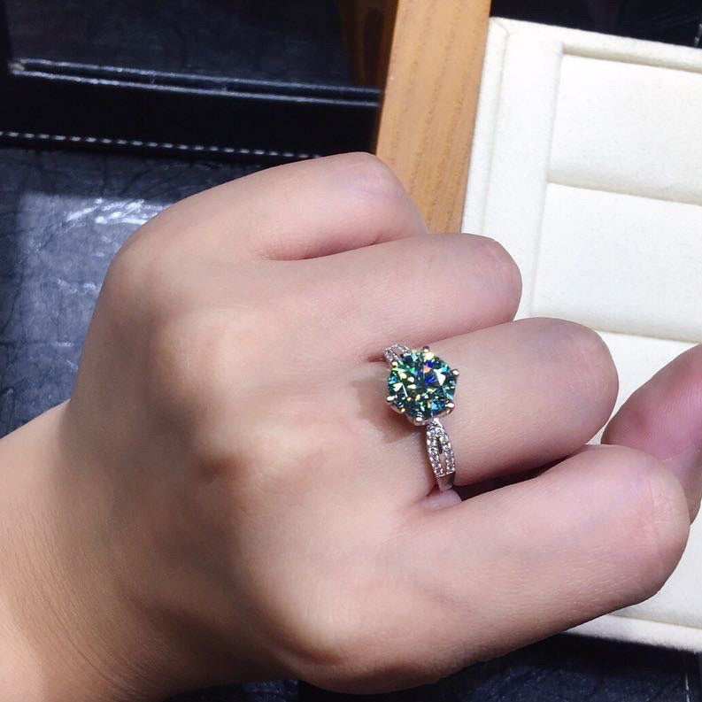 Hand wearing a ring with a colorful gemstone on a blurred background
