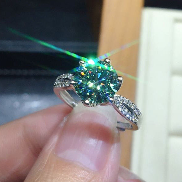 Ring with a large green gemstone held by a hand against a blurred background