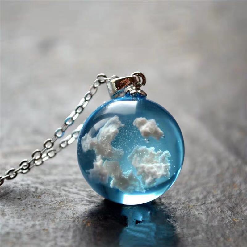 Necklace with a pendant featuring clouds inside a blue sphere on a gray surface