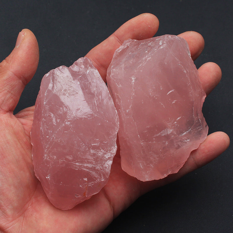 Two pink crystals held in a hand against a dark background