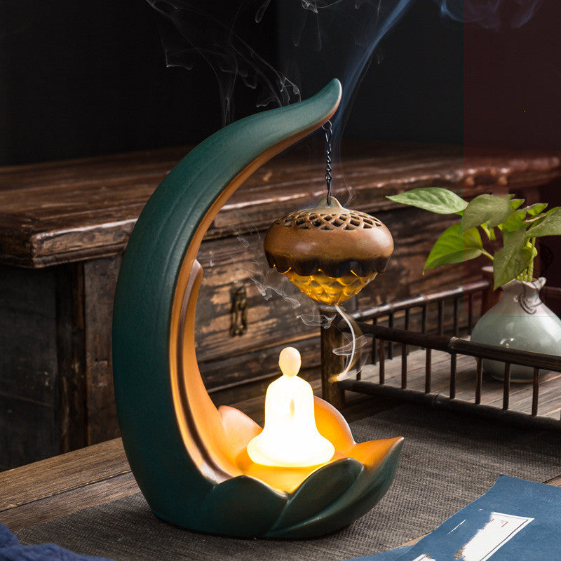 Decorative incense burner shaped like a crescent moon with smoke rising, set against a wooden table and background.
