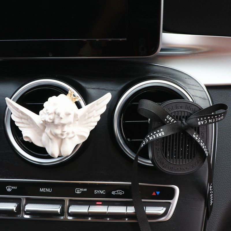 Car air freshener with an angel figurine and black ribbon on a car dashboard.