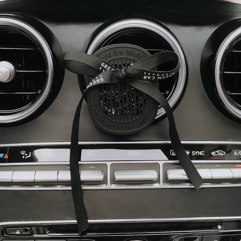 Car air freshener with a black strap hanging from the air vent.