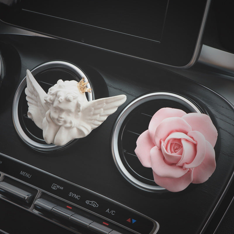 Decorative angel and rose car air freshener on a car dashboard.