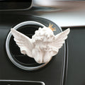 Decorative angel figure with wings and a crown on a car air vent.