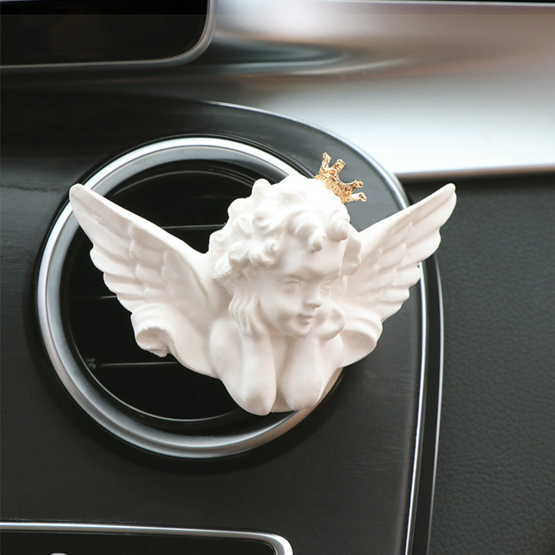 Decorative angel figure with wings and a crown on a car air vent.