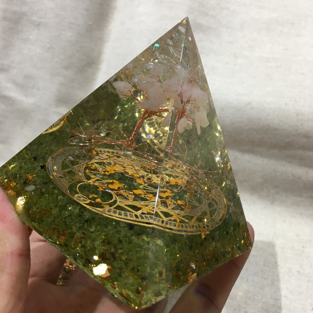 Green crystal pyramid with gold inlay held by a hand on a white background