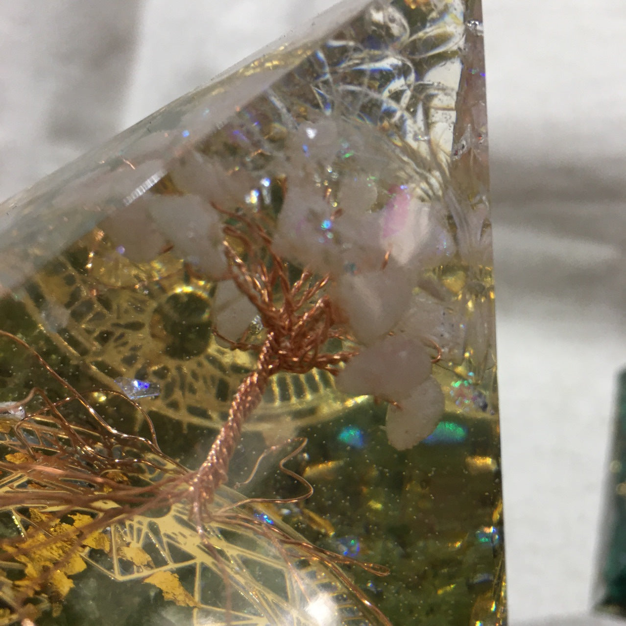 Close-up of a decorative item with gold wire, white flowers, and green elements in a clear resin-like material.