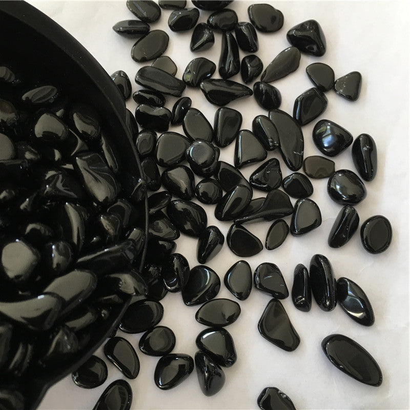 Black pebbles spilling out of a black container on a white surface