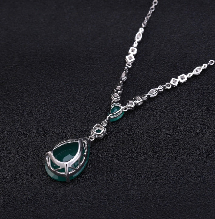 Silver necklace with a green teardrop pendant on a black background