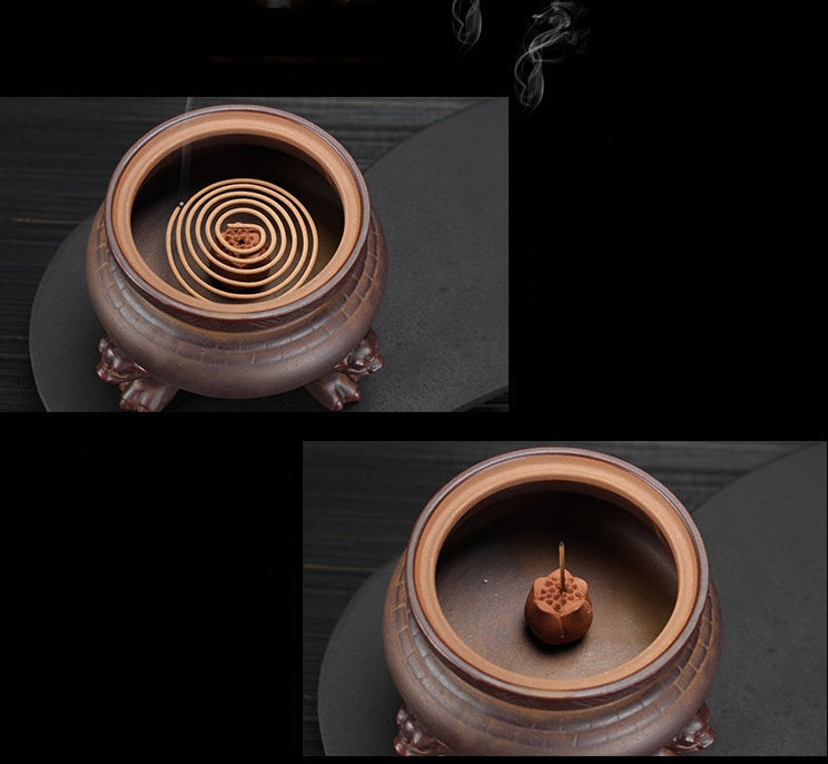 Ceramic incense burner with coiled incense and a single stick of incense on a dark background.