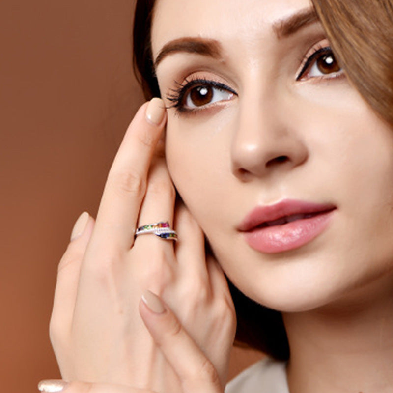 Close-up of a woman's face with a hand touching her cheek, wearing a colorful ring.