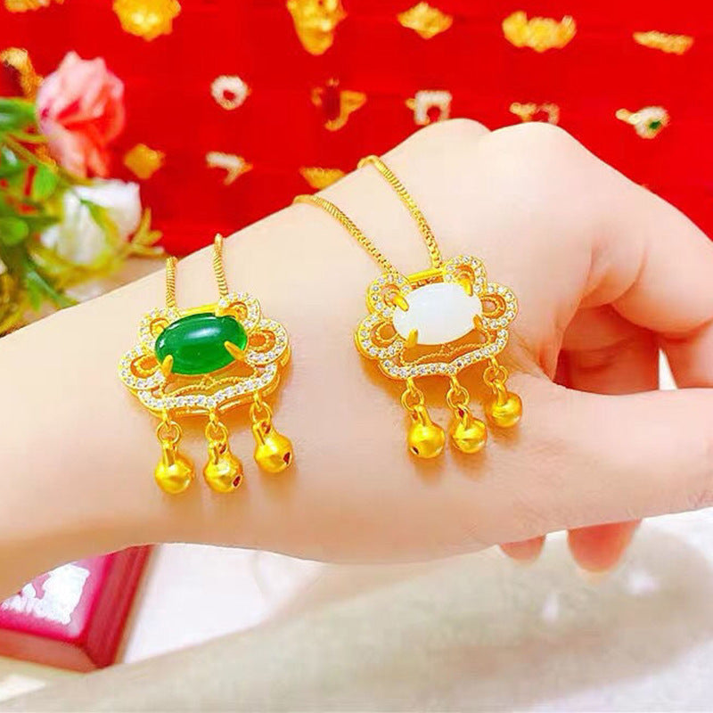 Gold necklaces with green and white stones held in a hand against a red floral background