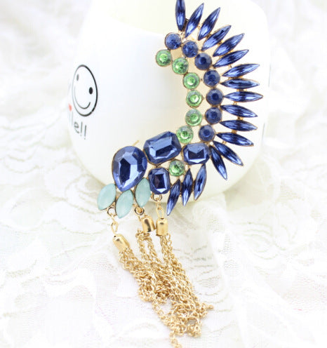 Decorative brooch with blue and green gemstones and gold tassel on a white background