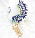 Decorative brooch with blue and green gemstones and gold tassel on a white background