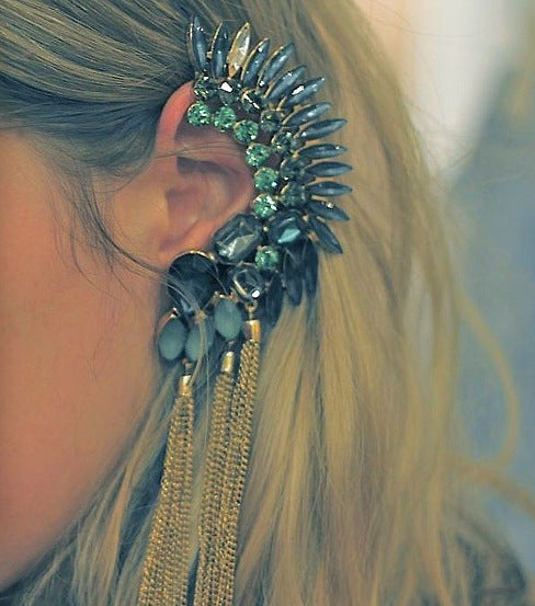 Close-up of an ornate earring with blue and gold elements worn by a person with blonde hair.
