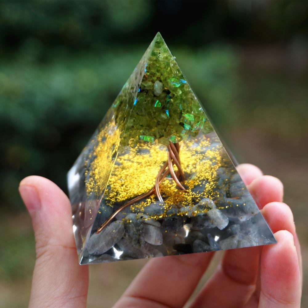 Triangular crystal with embedded tree and stones held by a hand against a blurred green background