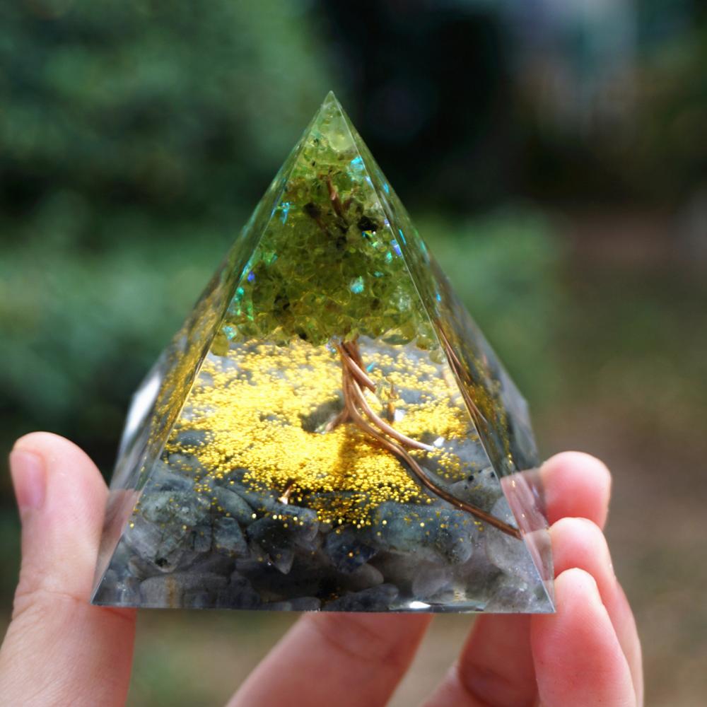 Pyramid-shaped crystal with yellow powder and small branches held by a hand against a blurred natural background