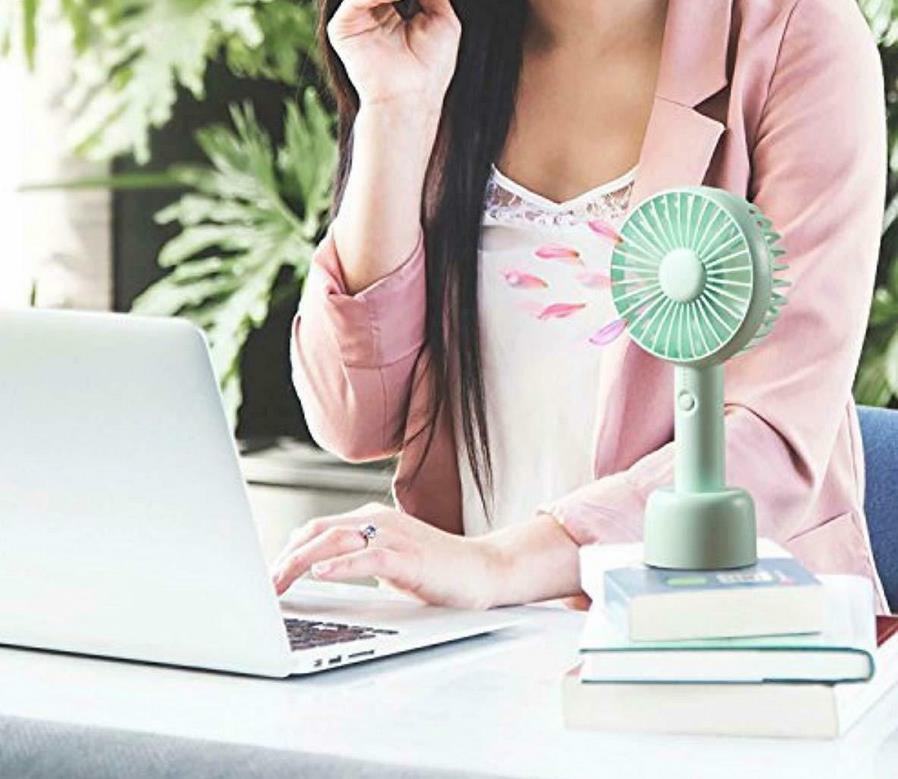 Person using a laptop with a small green fan on a stack of books