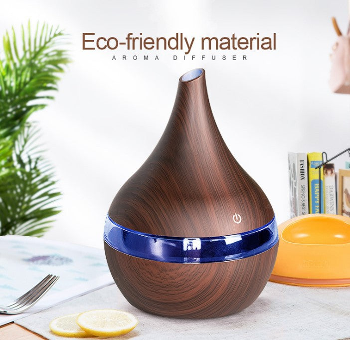 Wooden aroma diffuser with blue accents on a table with a plant and books in the background.