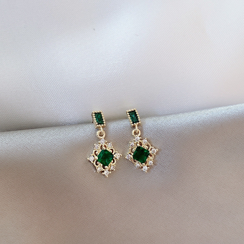 Pair of gold earrings with green gemstones on a light fabric background