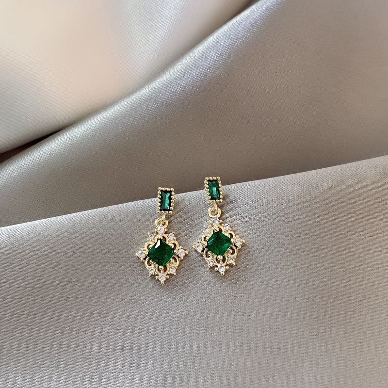 Pair of emerald green gemstone earrings on a light fabric background