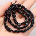 Black stone bead necklace held in a hand against a neutral background