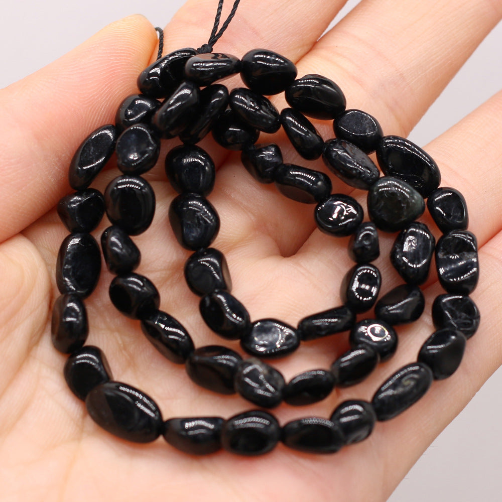 Black stone bead necklace held in a hand against a neutral background