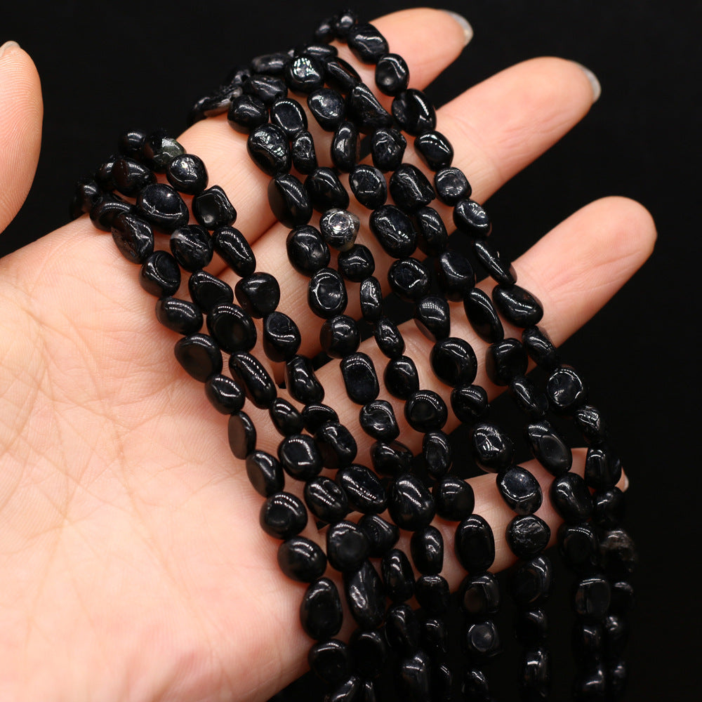 Black pebble necklace held in a hand against a black background