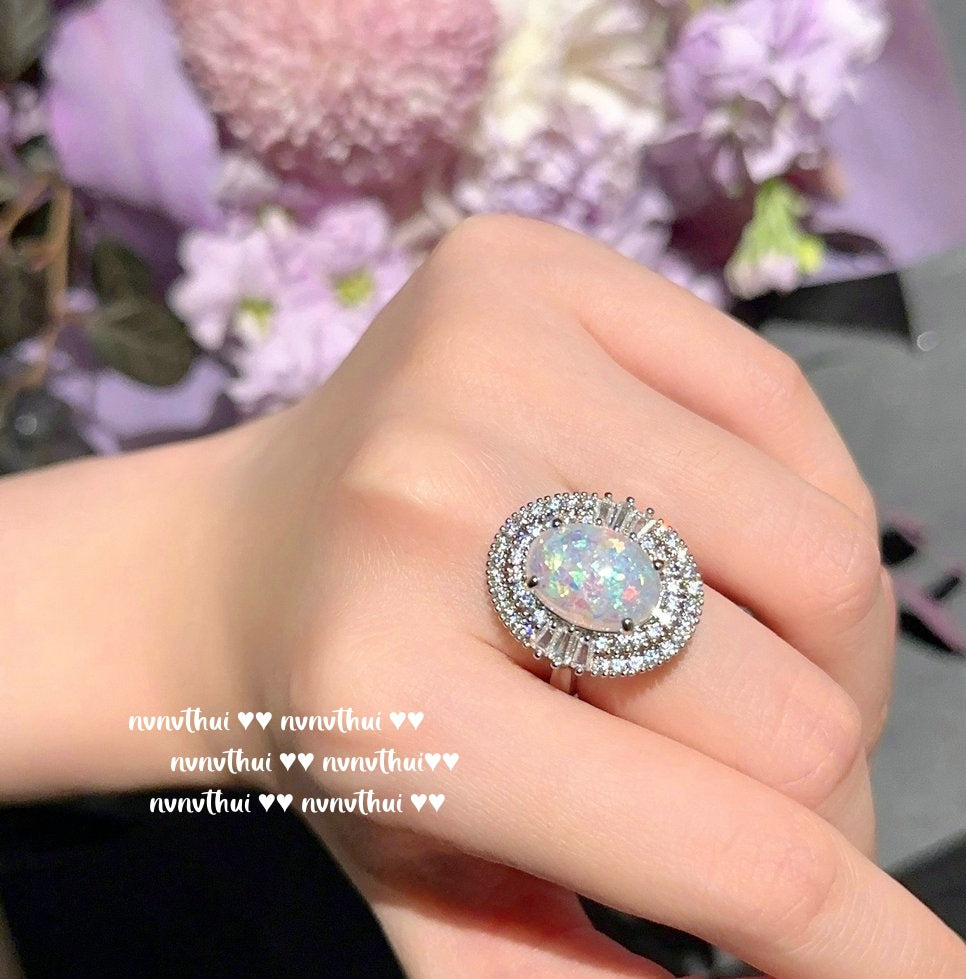 Hand wearing a ring with a colorful gemstone against a blurred floral background