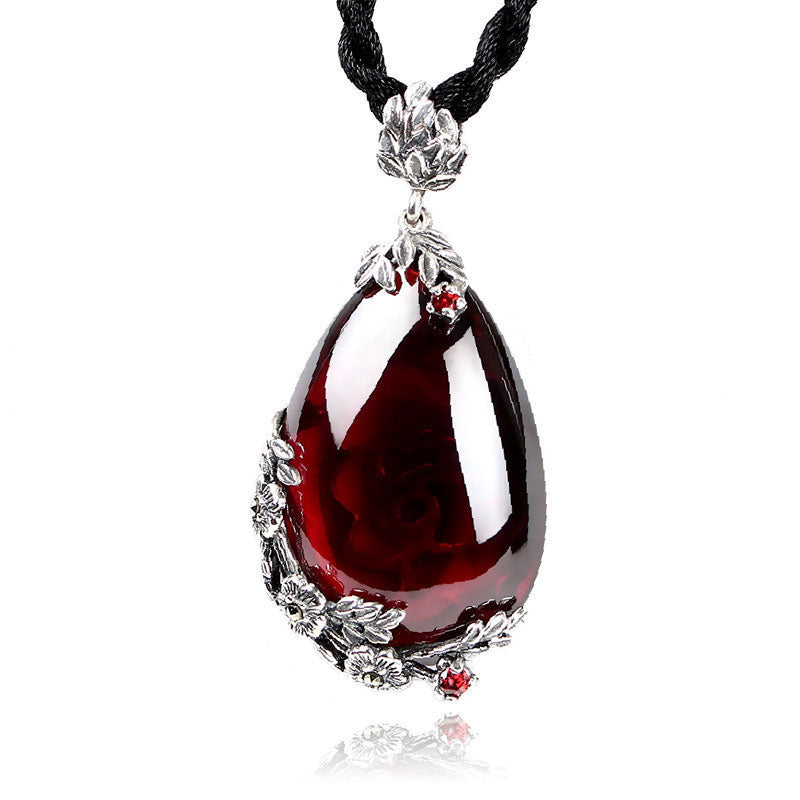 Teardrop-shaped red pendant with silver floral designs on a black cord against a white background