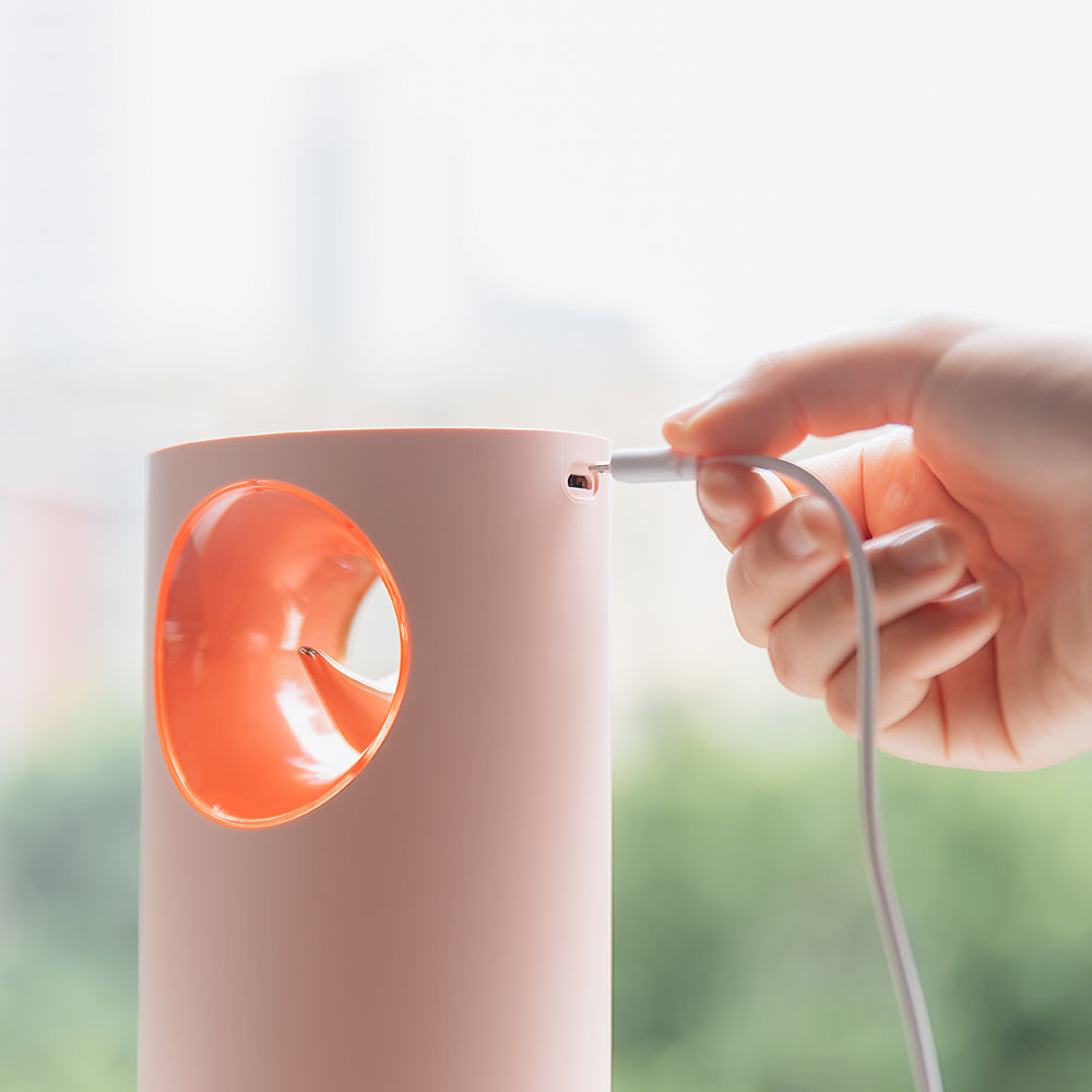 Person plugging a white cable into a pink lamp with an orange light bulb.