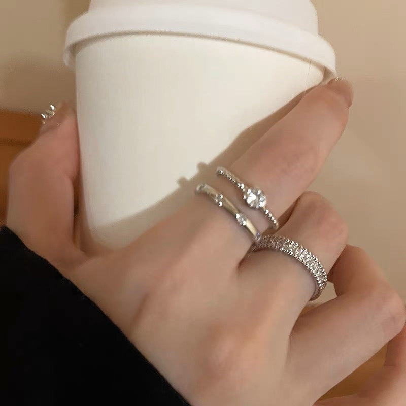 Hand holding a white cup with silver rings on fingers against a neutral background