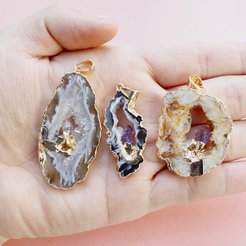 Three agate geode pendants with gold accents held in a hand against a pink background