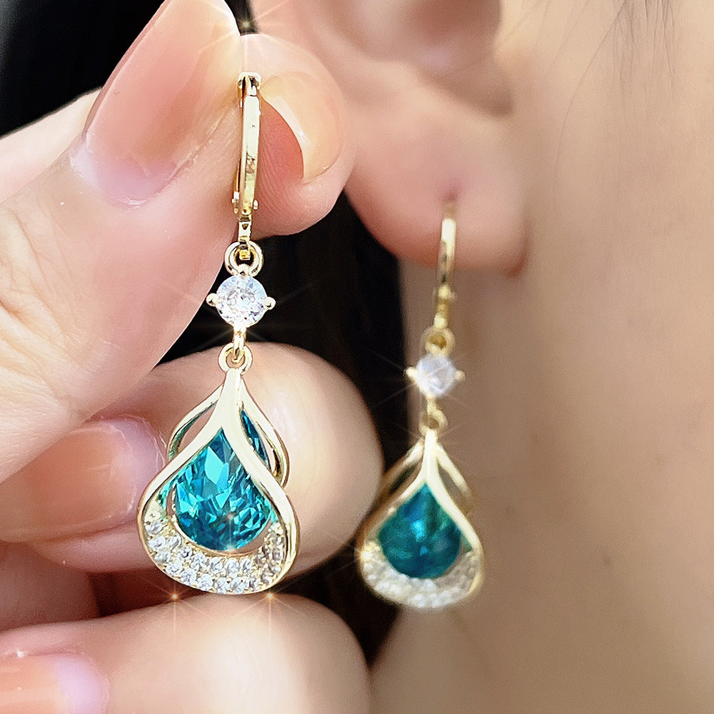 Teardrop-shaped earrings with blue gemstones and gold accents held near an ear.