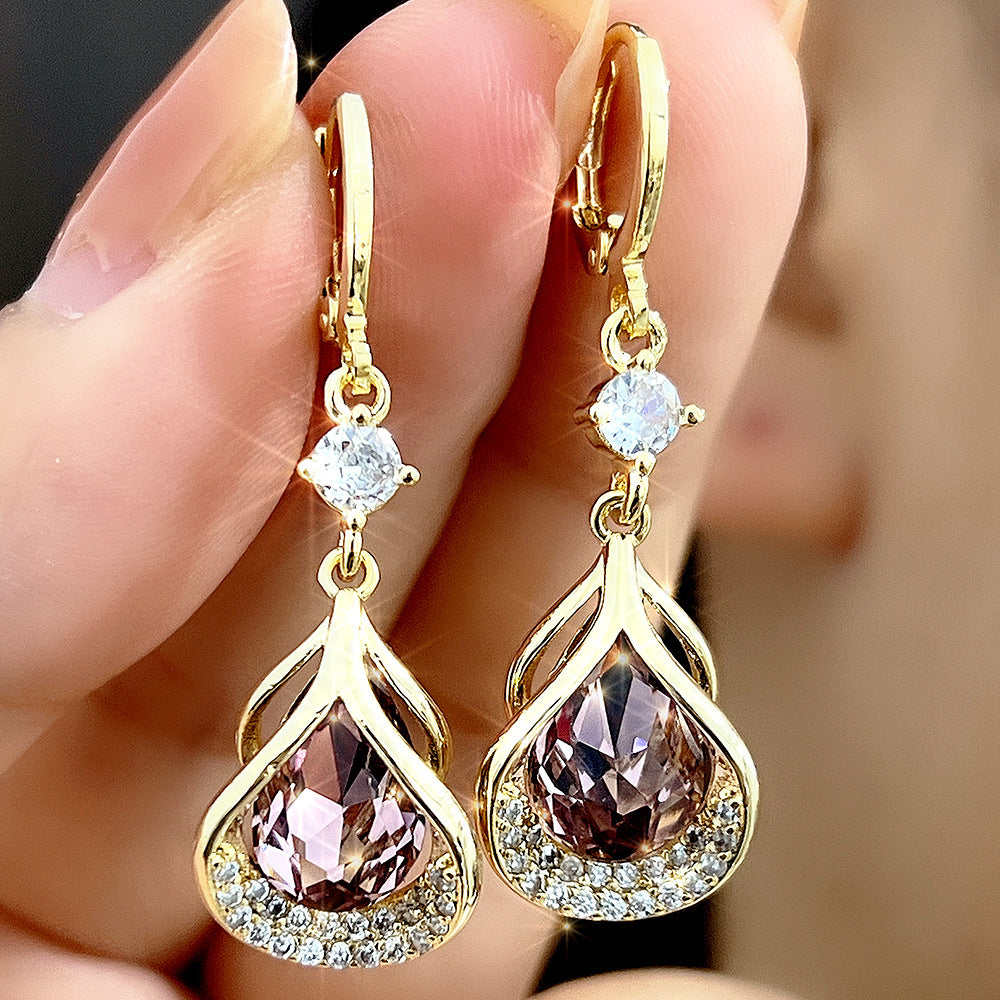 Gold earrings with teardrop-shaped gemstones held between fingers against a blurred background