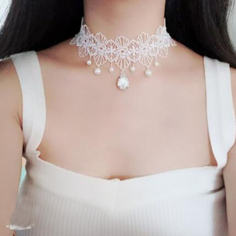 White lace choker necklace with pearls on a person wearing a white top.