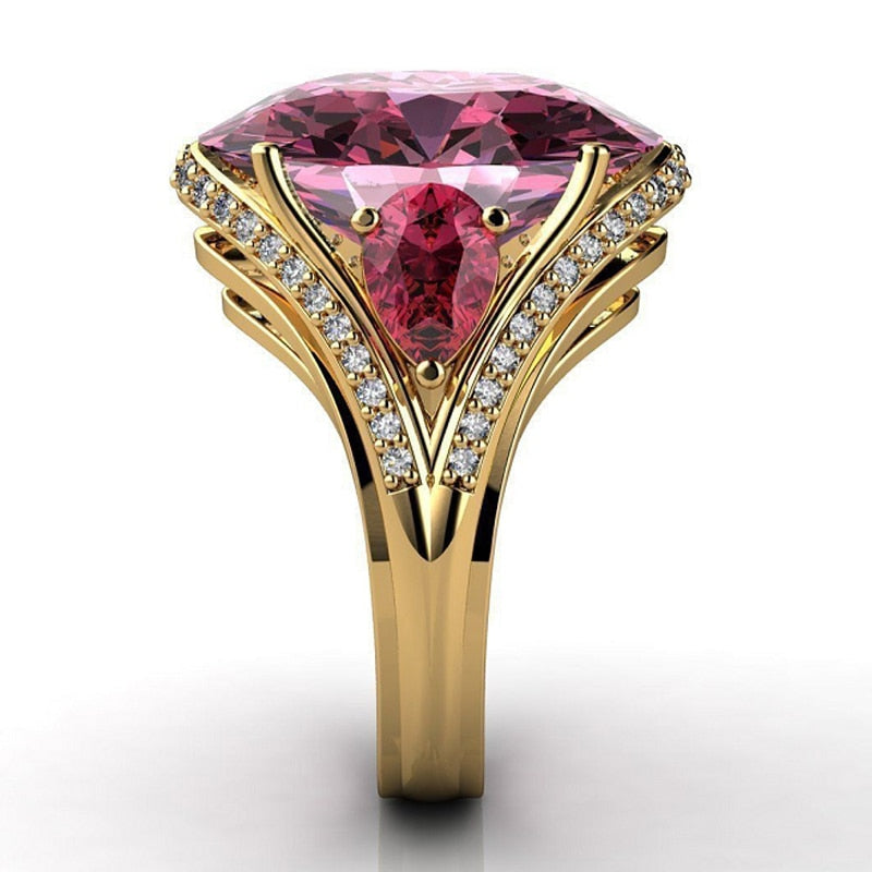 Gold ring with a large pink gemstone and smaller diamonds on a white background