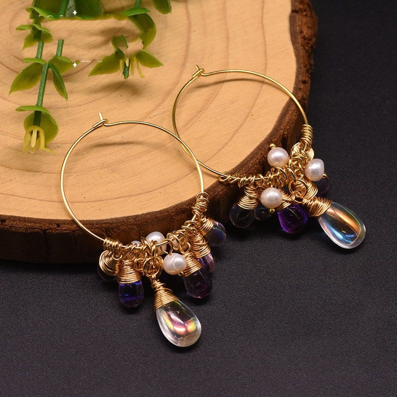 Gold hoop earrings with pearls and purple beads on a wooden surface