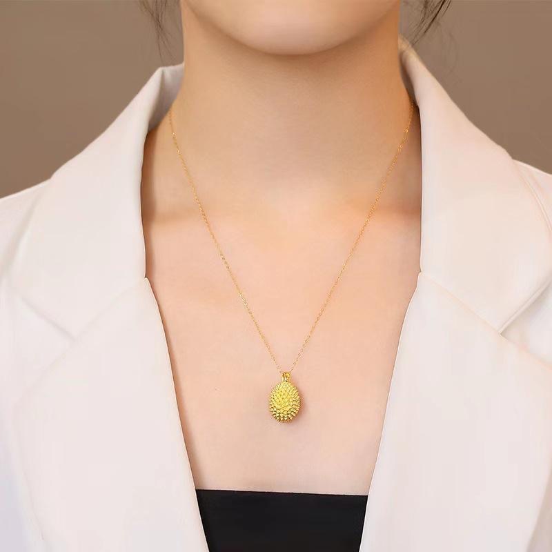 Gold necklace with a unique pendant worn by a person against a neutral background
