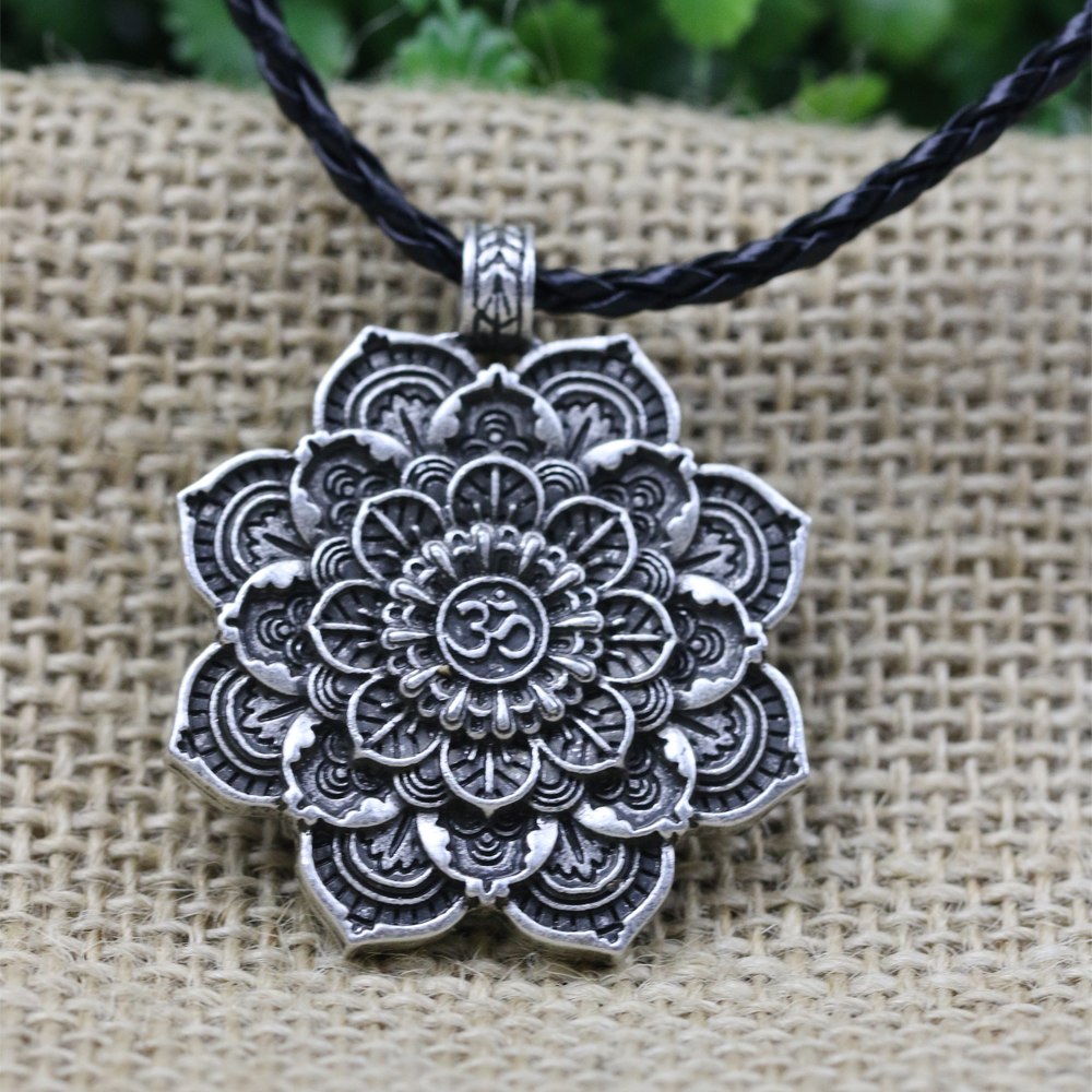Silver mandala pendant with 'Om' symbol on a black cord against a textured beige background
