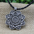 Silver mandala pendant with 'Om' symbol on a black cord against a textured beige background