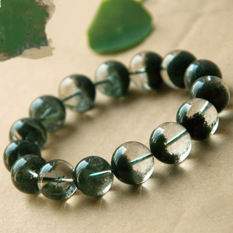 Green beaded bracelet on a textured beige surface with green leaves in the background