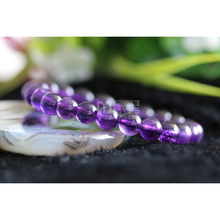 Purple beaded bracelet on a dark surface with a blurred natural background