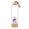 Clear glass water bottle with wooden top and bottom, containing purple and clear crystals.