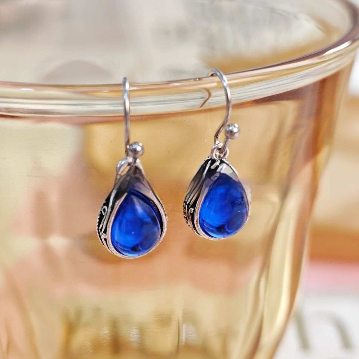 Blue teardrop earrings with silver hooks on a glass surface