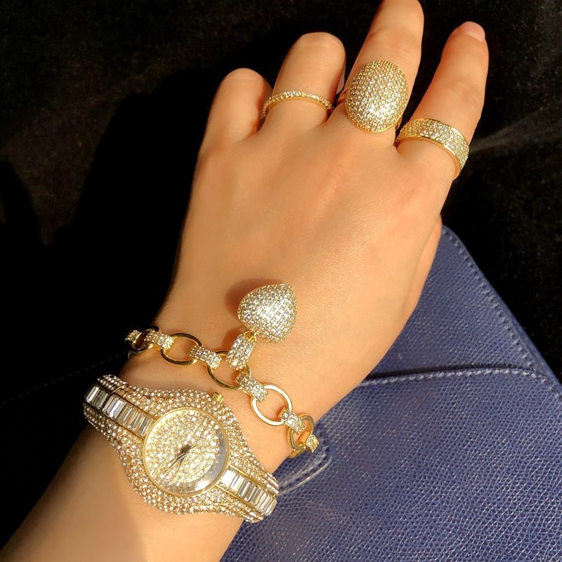 Hand wearing a gold watch and multiple gold rings on a dark background