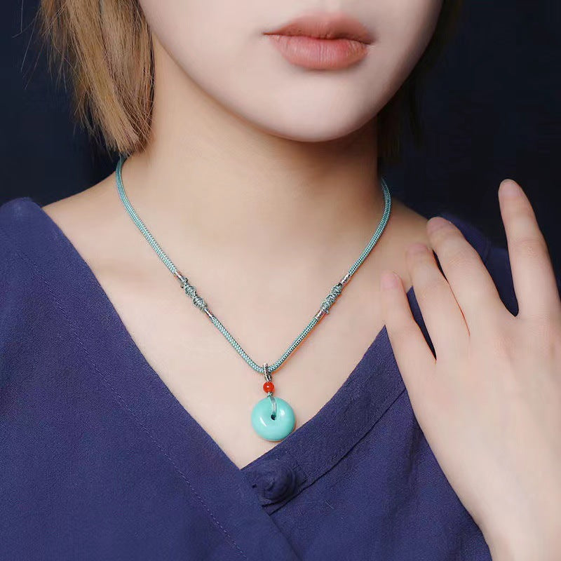 Necklace with a turquoise pendant worn by a person in a dark blue outfit.
